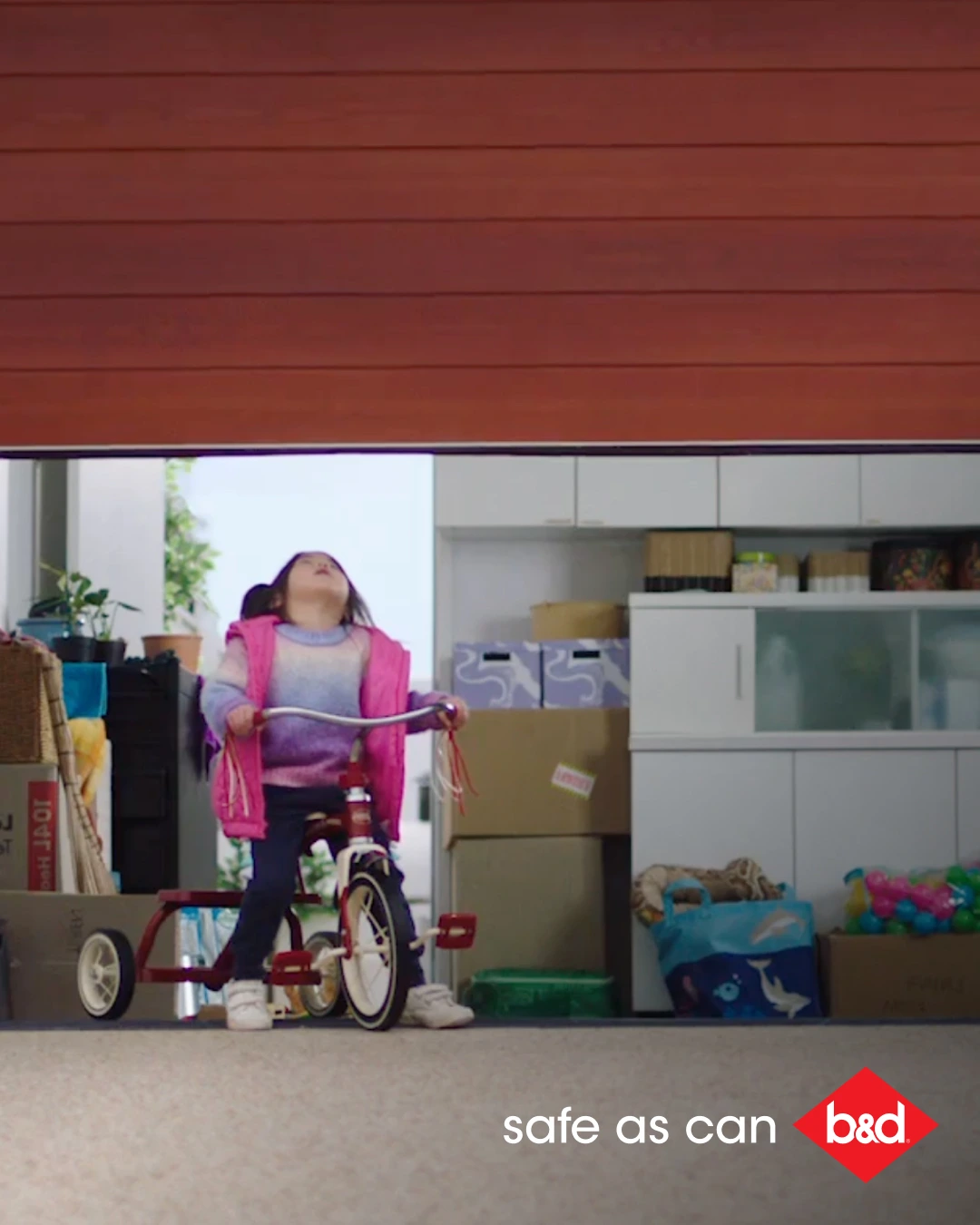 Safe as Can B&D - Small girl riding cycle heading towards closing garage door
